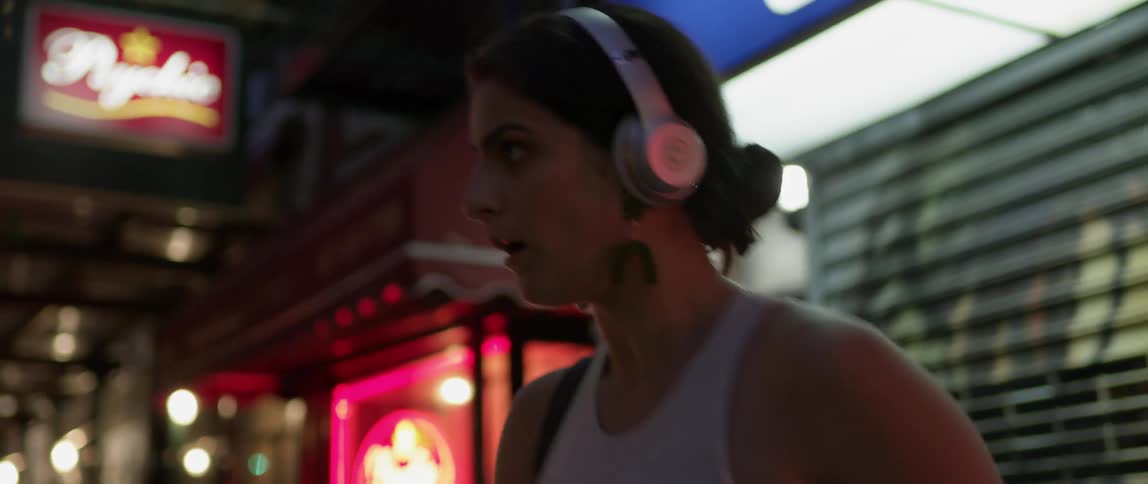A woman wearing headphones dances on a city sidewalk at night