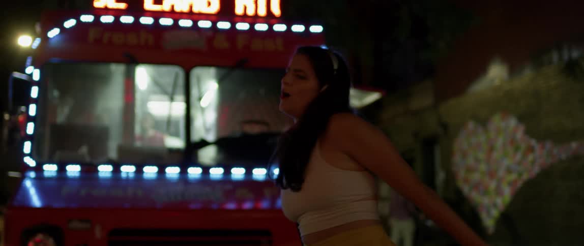 Woman dances by a truck lit up by neon at night