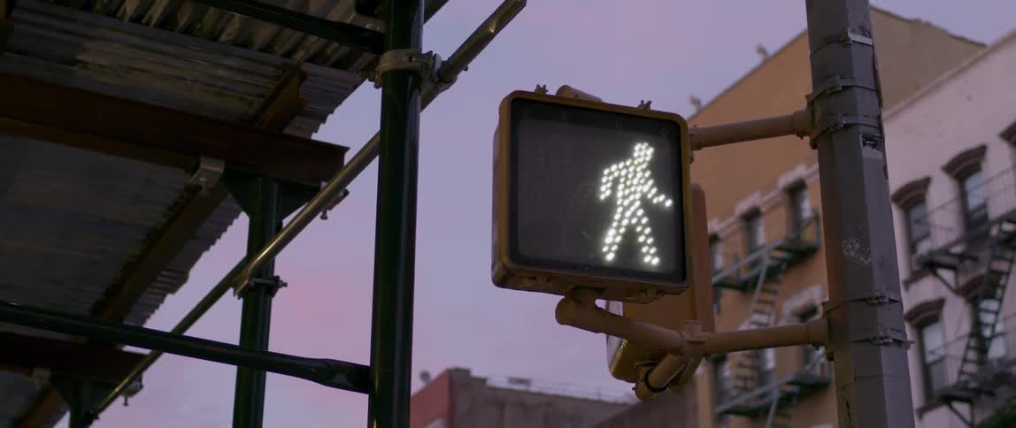 A crosswalk signal is displaying the walk symbol at dusk