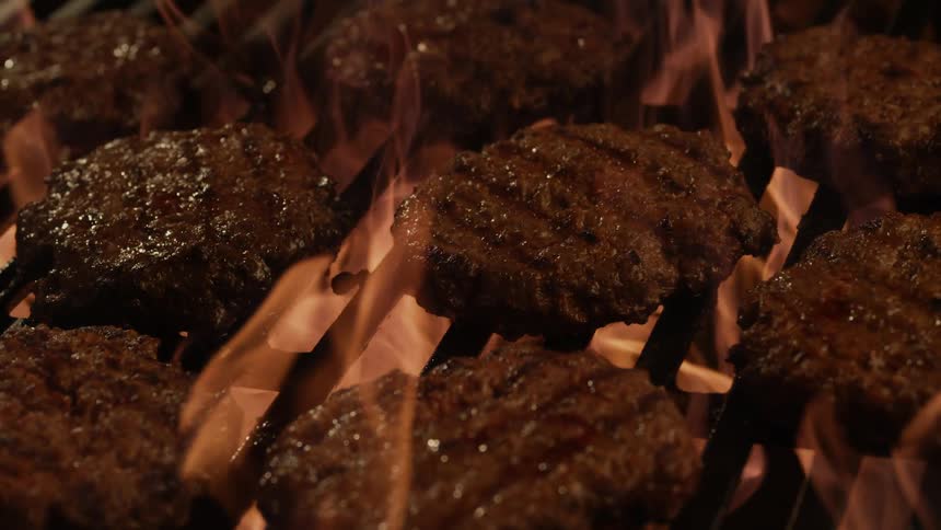 Hamburgers are cooked on a flaming grill