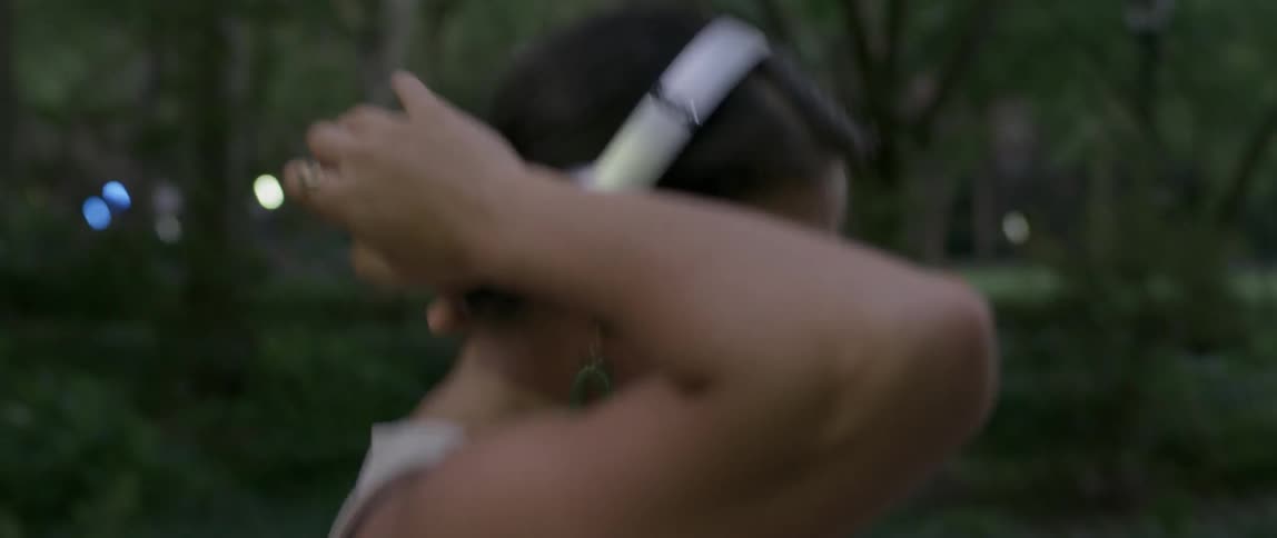 A woman dances outside with headphones on