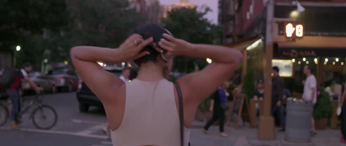 Woman puts her hair up while dancing and walking across a city street