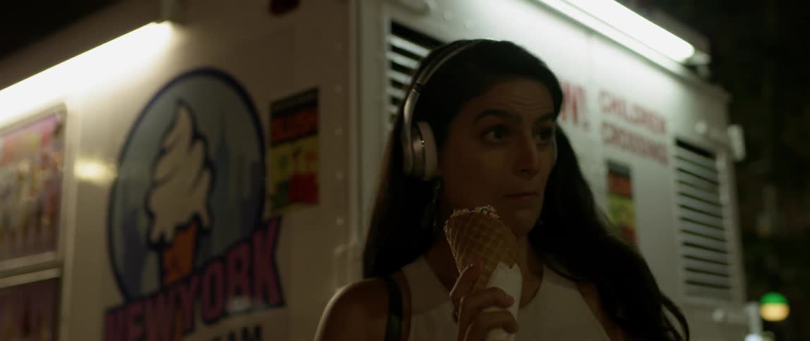 Woman wearing headphones stands next to an ice cream truck eating an ice cream cone