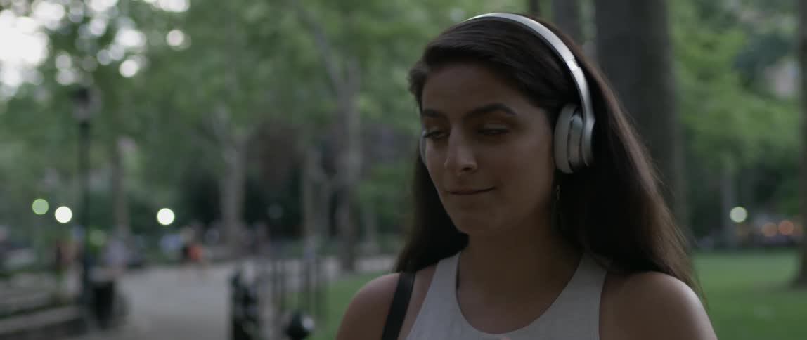 Woman wearing headphones stands in a park smiling and nodding
