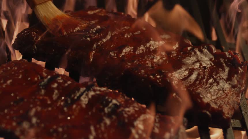 Barbecue sauce being applied to ribs while they are grilling