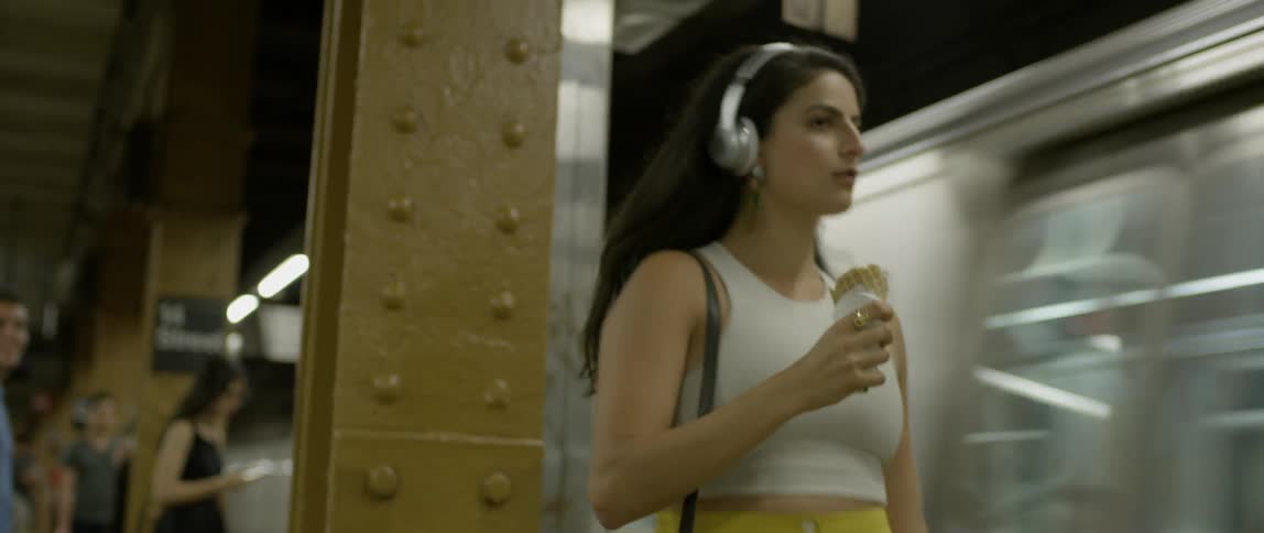 A woman dances and sings while eating an ice cream cone at a subway station