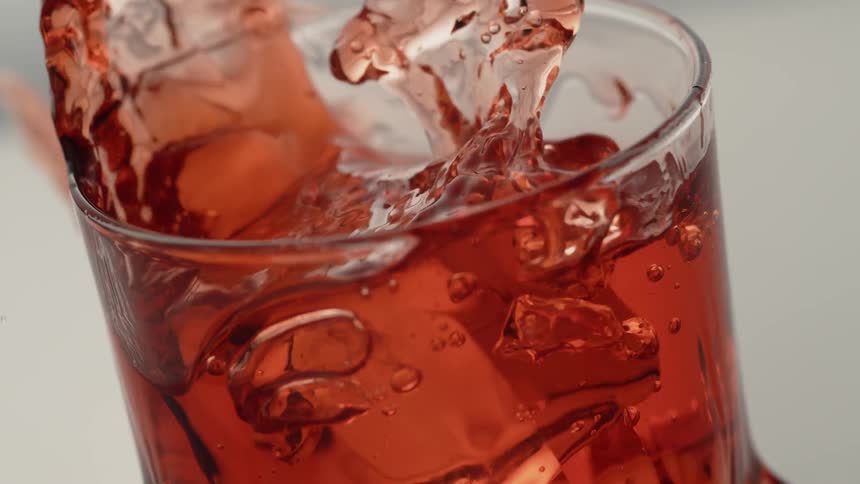 An ice-cube is splashing into a red beverage