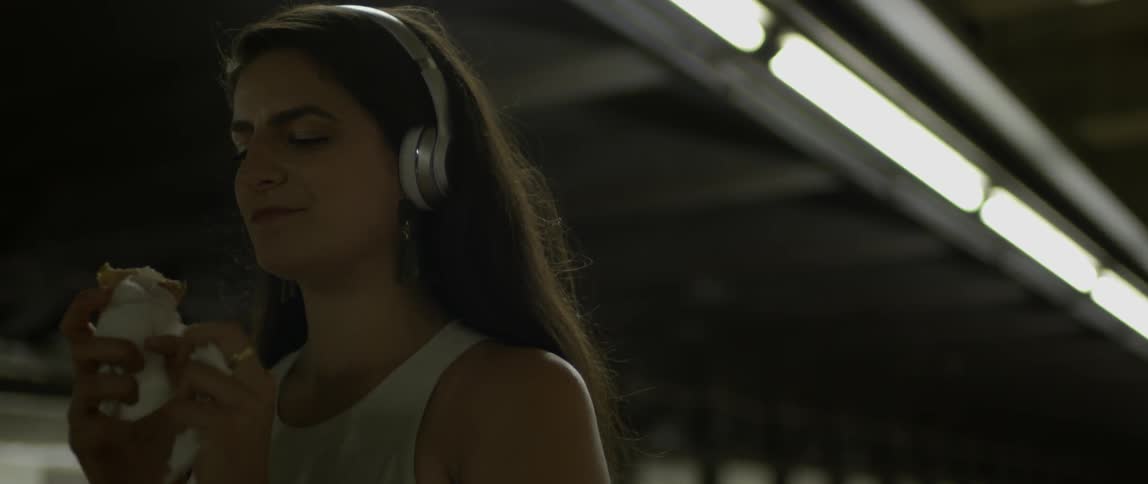 A woman eats an ice cream cone with headphones on