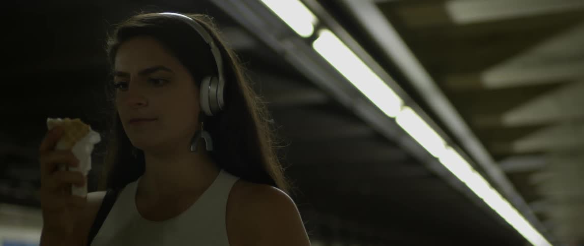 A woman eats an ice cream cone with headphones on
