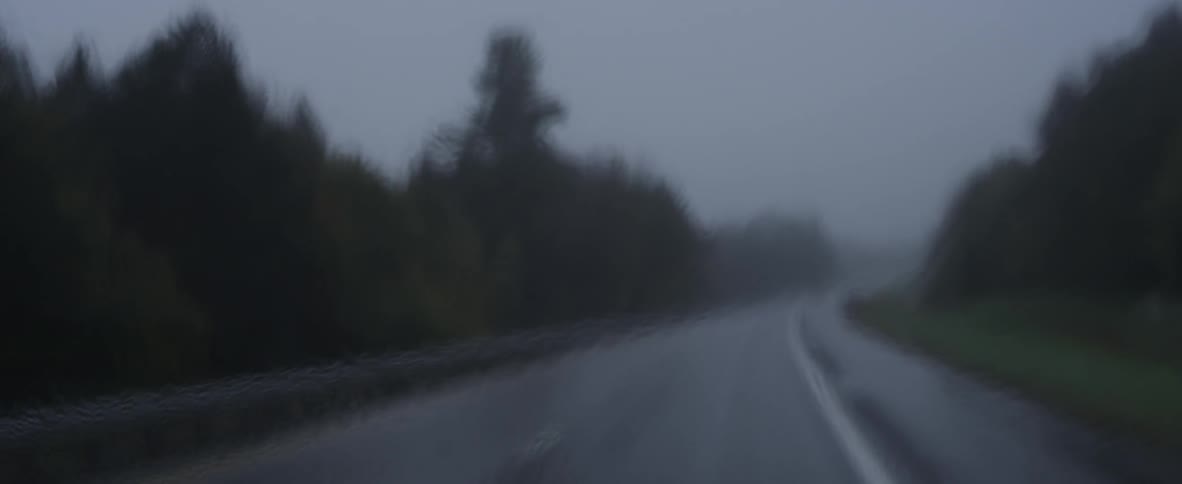 A rain soaked road as seen through a windshield