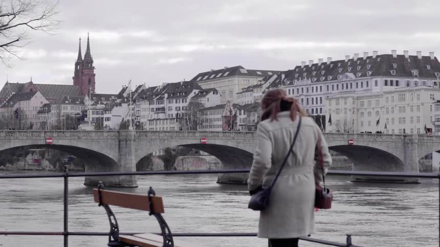 A woman walks past the water and sits on a bench
