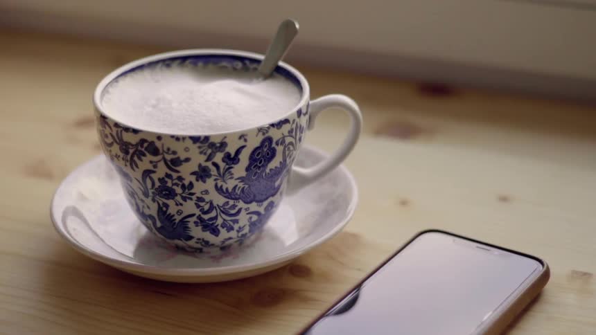 A phone sits next to a cup of coffee