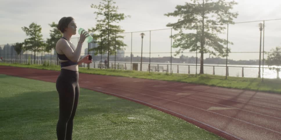 Woman stands in the middle of a track field drinking water