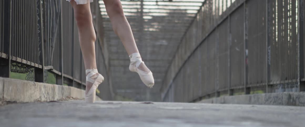A ballerina is dancing on a bridge outside in daylight