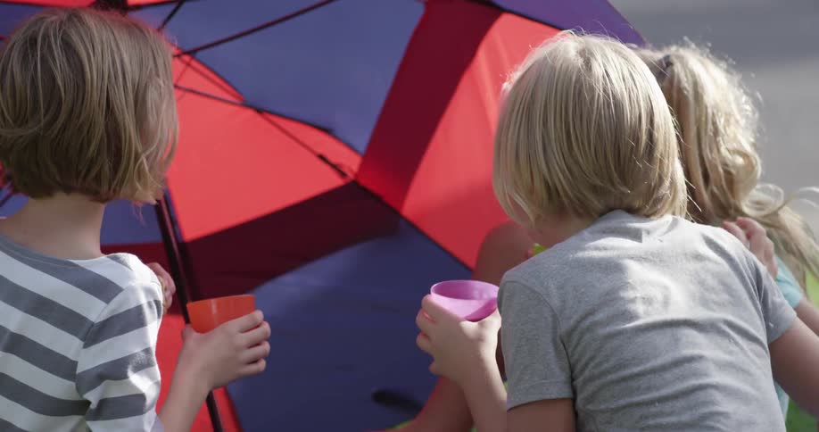 Kids sit under an umbrella and eat snacks