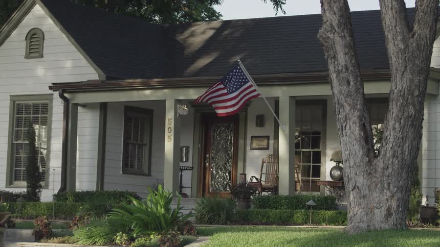 A clean and well-kept single-story home in a suburban neighborhood flies the american flag
