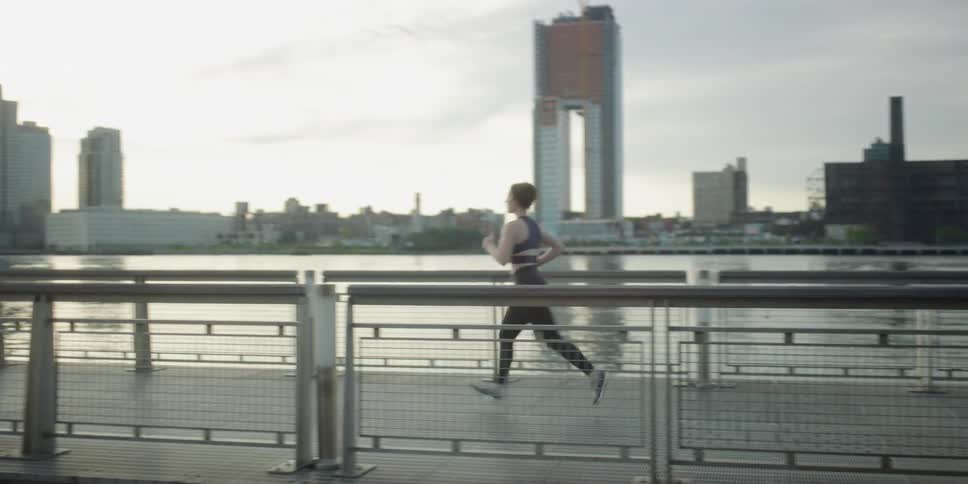 A woman jogs across a pedestrian bridge