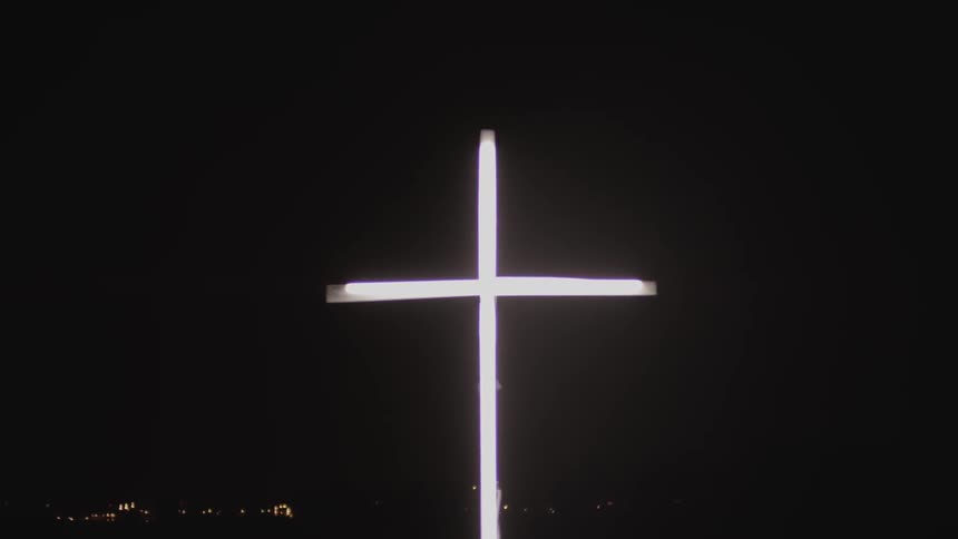 A cross is illuminated against a black sky