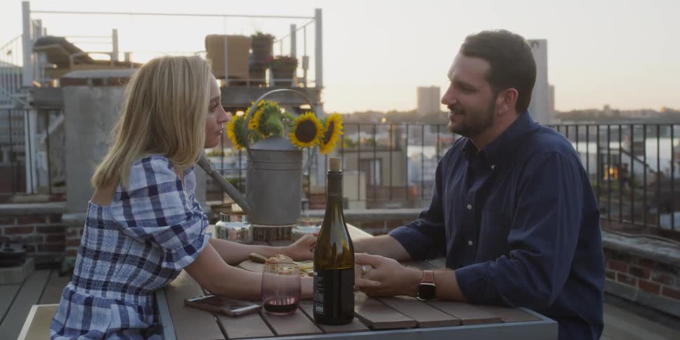 A man and woman are holding hands across a table on a porch in daylight