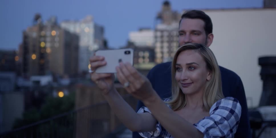 Man and woman take a picture on a building rooftop at dusk