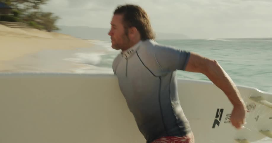 Man runs as he carries a surfboard from the water to the shore