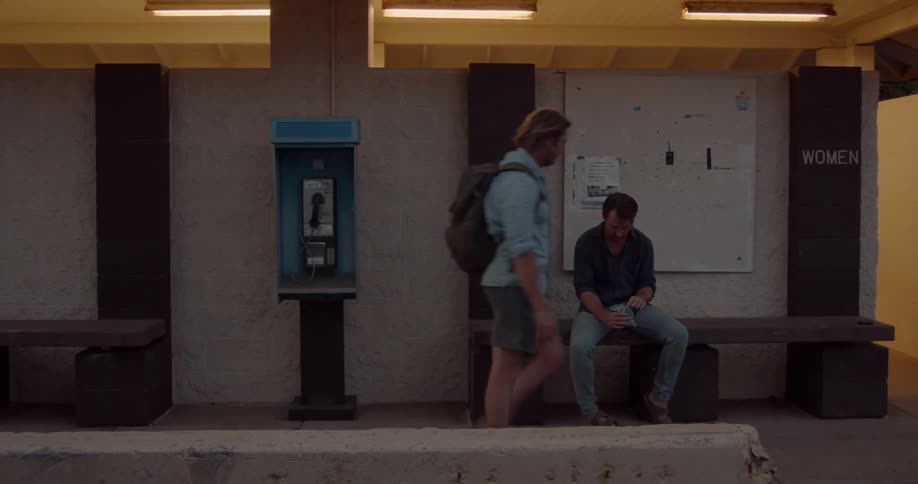 Man uses a payphone near another man at a train station
