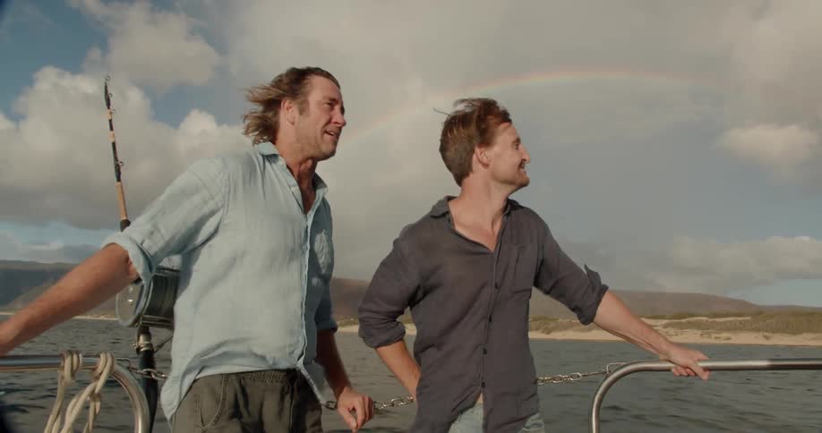 Two men are talking and laughing while riding on boat on cloudy day