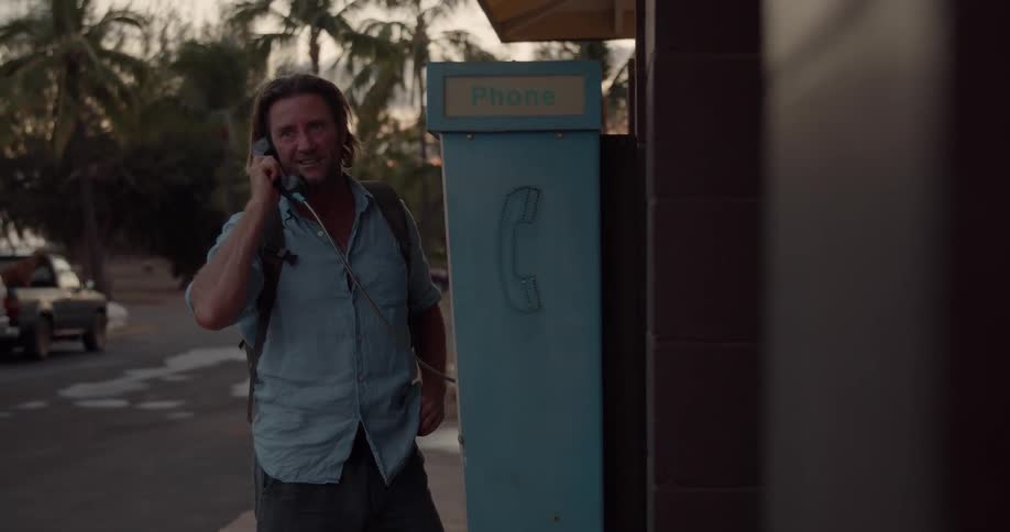A man uses a pay phone outside by the street