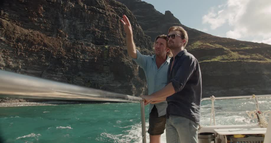 Two men stand on a boat talking and pointing upwards