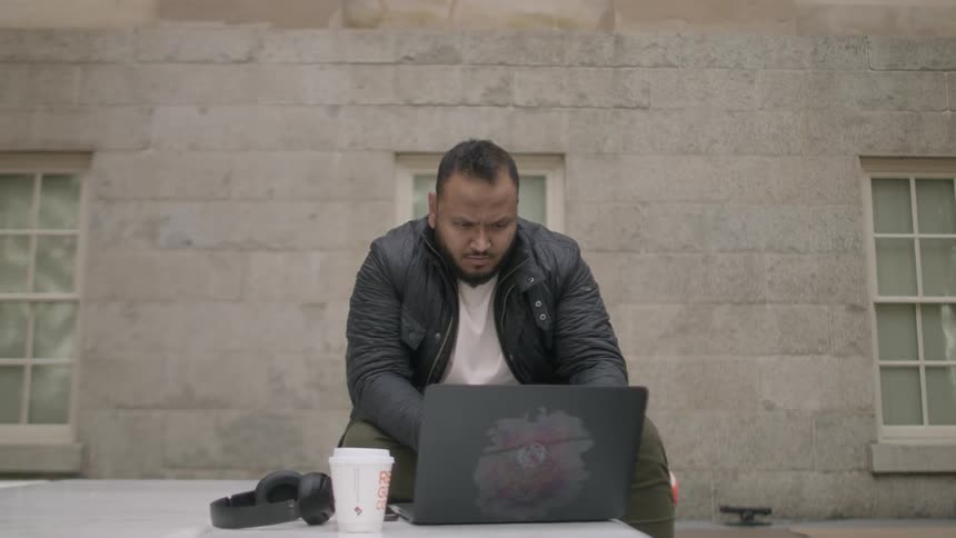 Man works on a laptop outside of a brick building