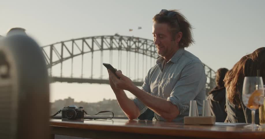 Man smiles at his cellphone as he sits at a table