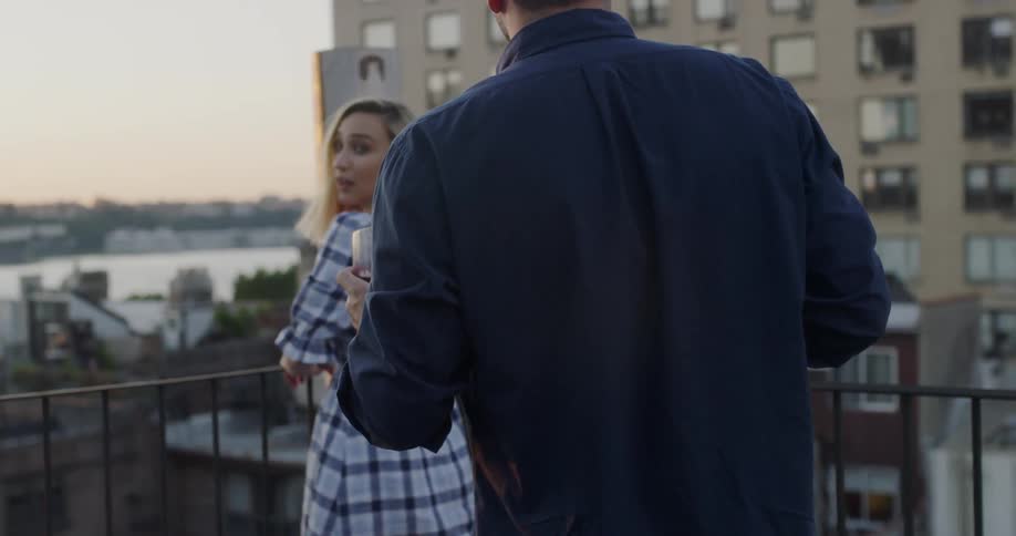 A man hands a woman a drink on the roof