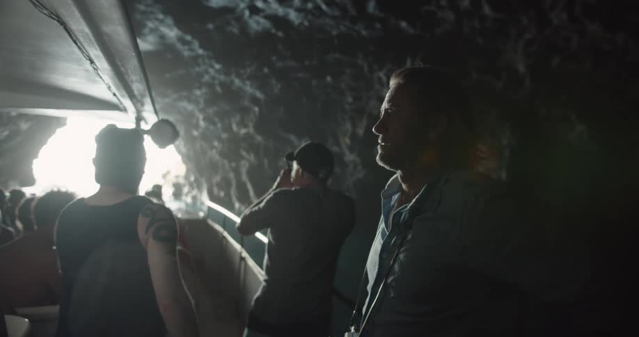 People riding through a tunnel-like cave on a boat together as they head towards the daylight at the cave exit