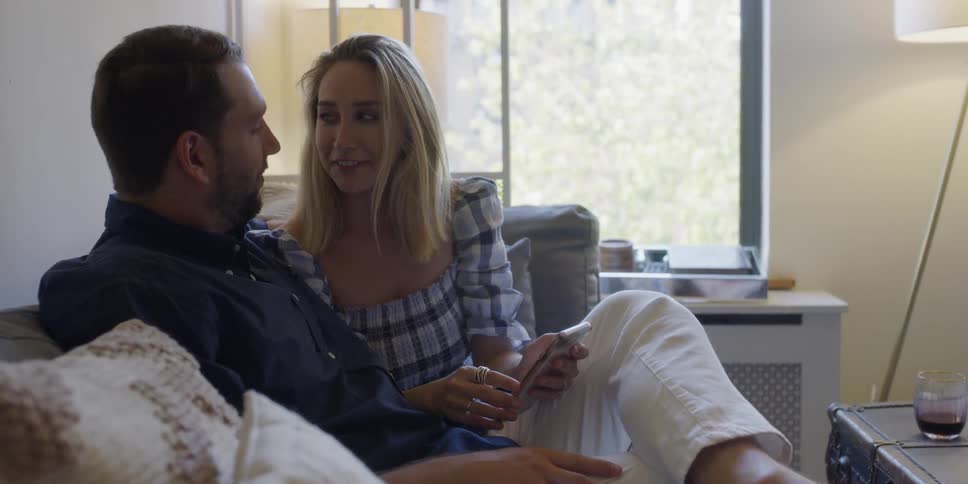 Man and woman sitting on a couch looking at a phone while talking