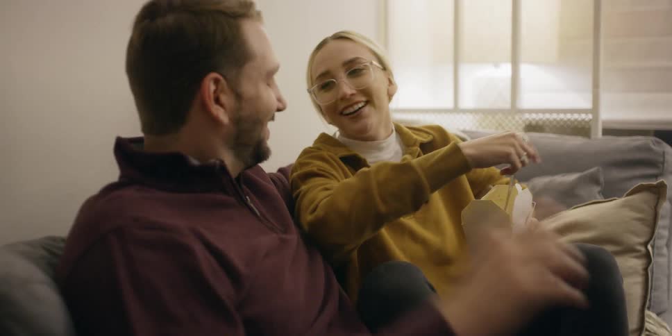 Man and woman laugh as they sit on a sofa