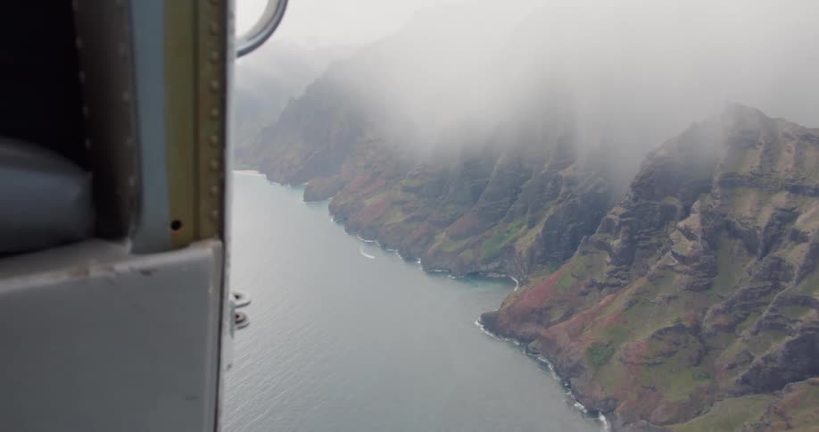 A helicopter flies above the water and mountains
