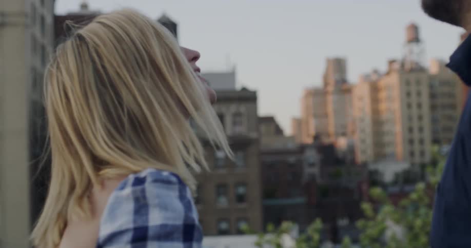 Woman smiles as a man hands her a glass of wine while standing on a balcony in the city