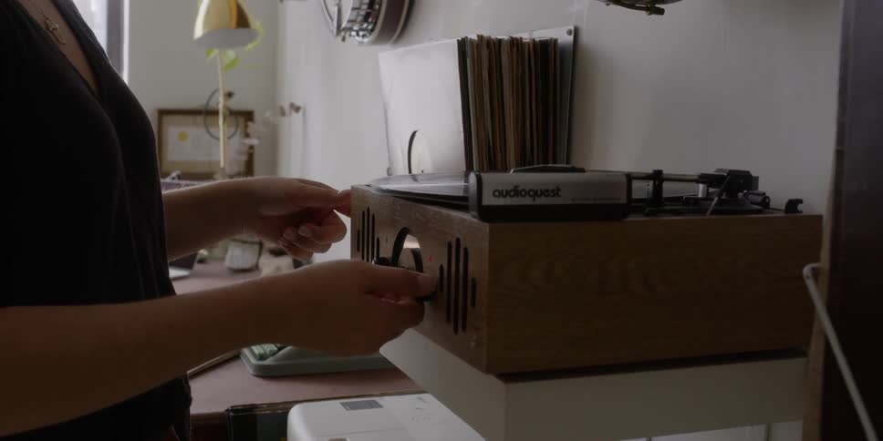 A woman lifts a record and puts it on the player