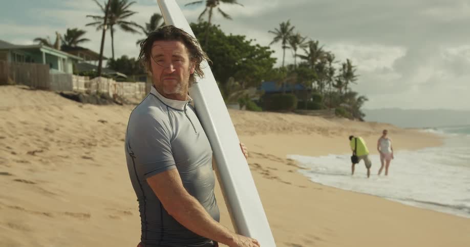 A man is standing on the beach holding a surfboard in daylight