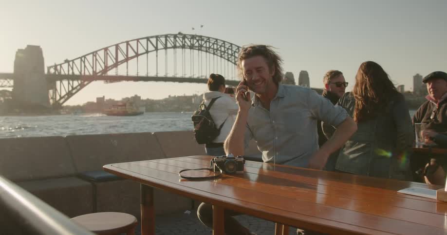 Man talks on the phone next to a city river at sunset