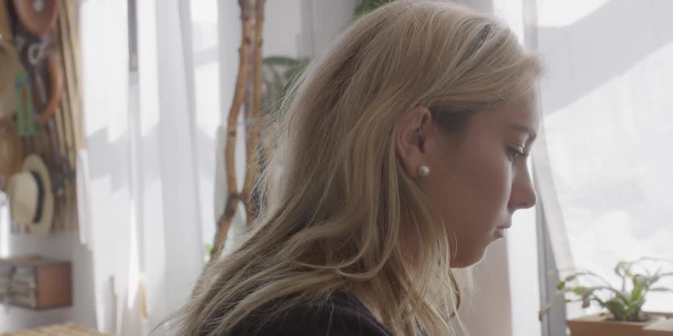 A blond haired woman brushes her hair behind her ear