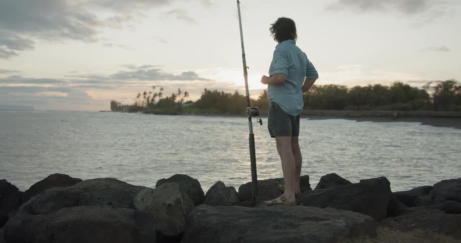 A man stands on the rocks by a fishing rod