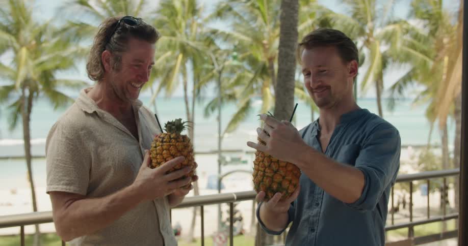 Two men are toasting with tropical drinks outside at the beach on a sunny day