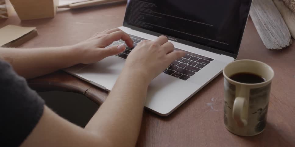 Woman is typing on laptop at desk and drinking coffee