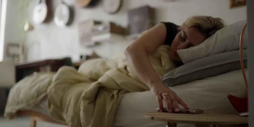 A woman rolling over in bed to grab her phone