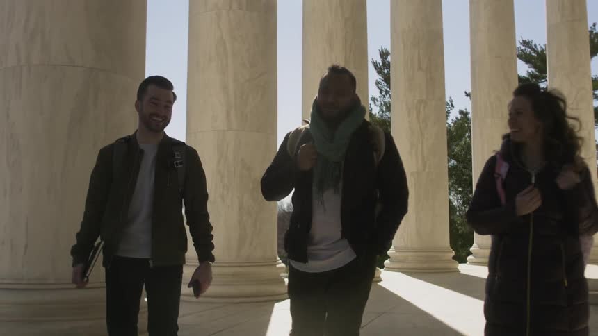Three people walk by the large columns