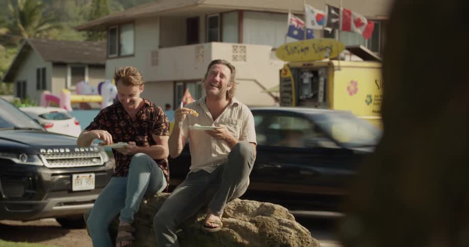 Two men are sitting outside talking and eating in sunny town