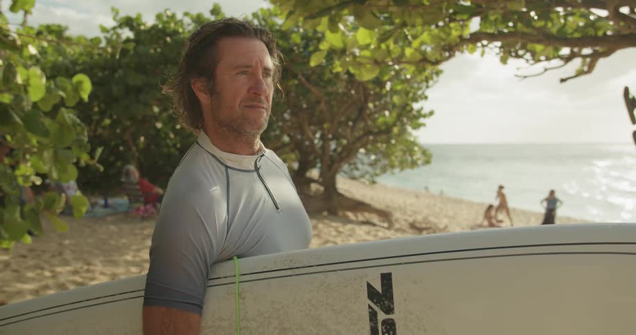 Man holds a surfboard standing on a beach and walks away