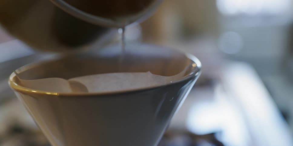 Pitcher of water pours steaming into a coffee filter