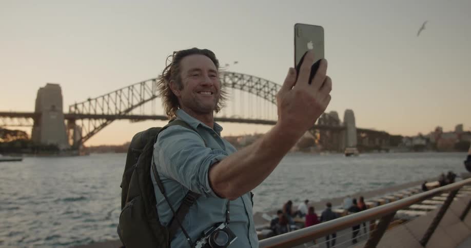A man makes a video call in front of a city bridge at sunset